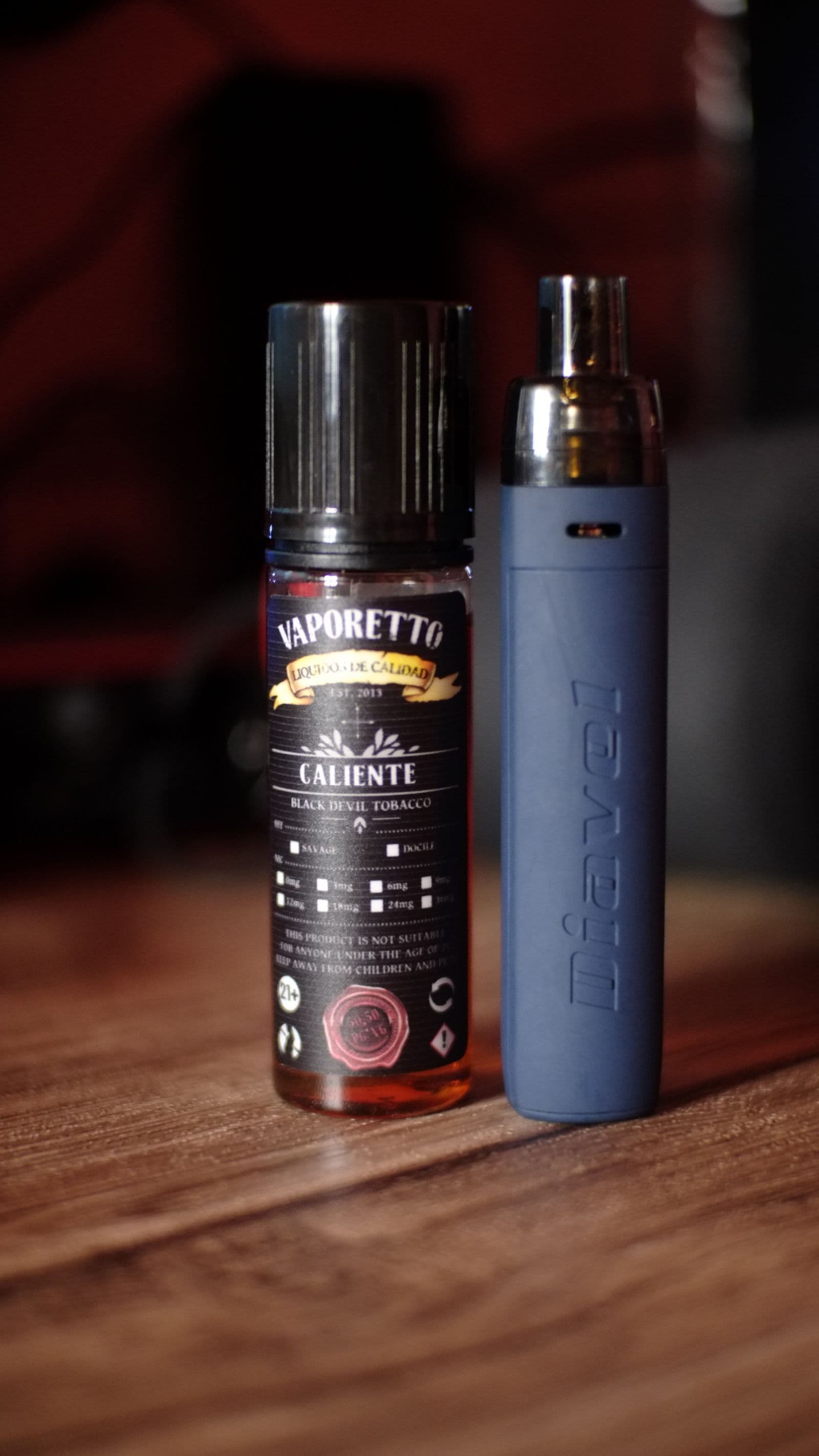 An e-liquid bottle beside a pod device on a wooden counter